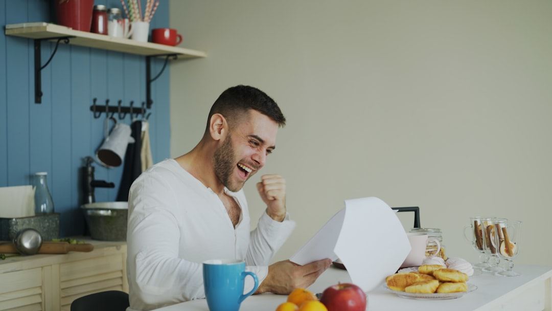 A person smiling over paperwork at a kitchen table with a cup of tea