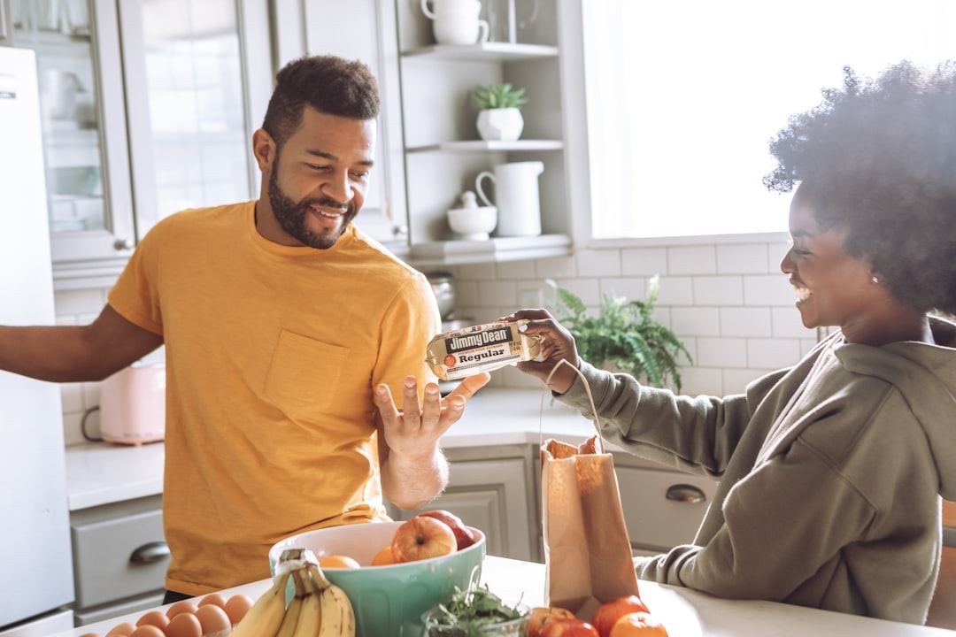 Two people unpacking groceries together in a bright kitchen, sharing a joke