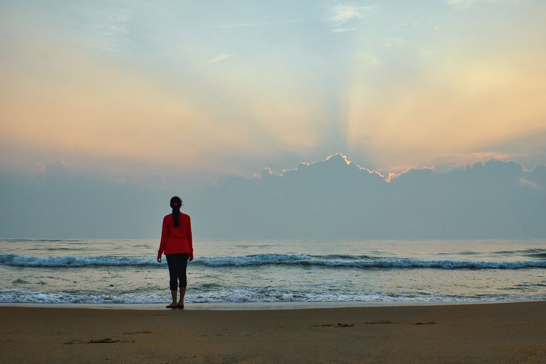 A person standing quietly by the ocean at dawn, looking out at a soft pastel sky